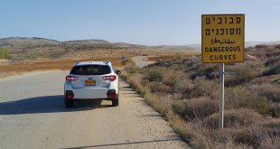 סובארו לבנה עומדת על כביש ליד שטח סיבובים מסוכנים