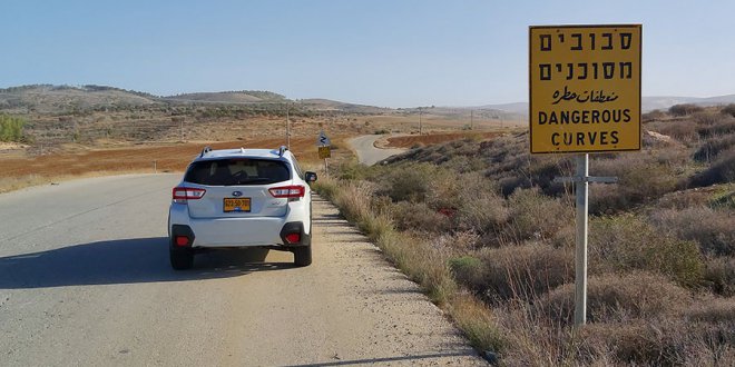 סובארו לבנה עומדת על כביש ליד שטח סיבובים מסוכנים